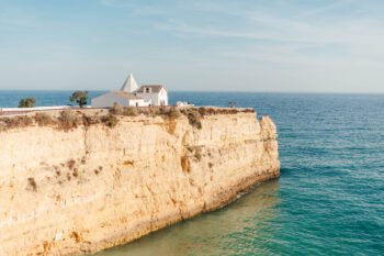 The iconic white chapel of Nossa Senhora da Rocha standing alone on a cliff promontory with the ocean surrounding it. Iconic white chapel (Nossa Senhora da Rocha) on a cliff promontory over the ocean, Algarve wedding venue.